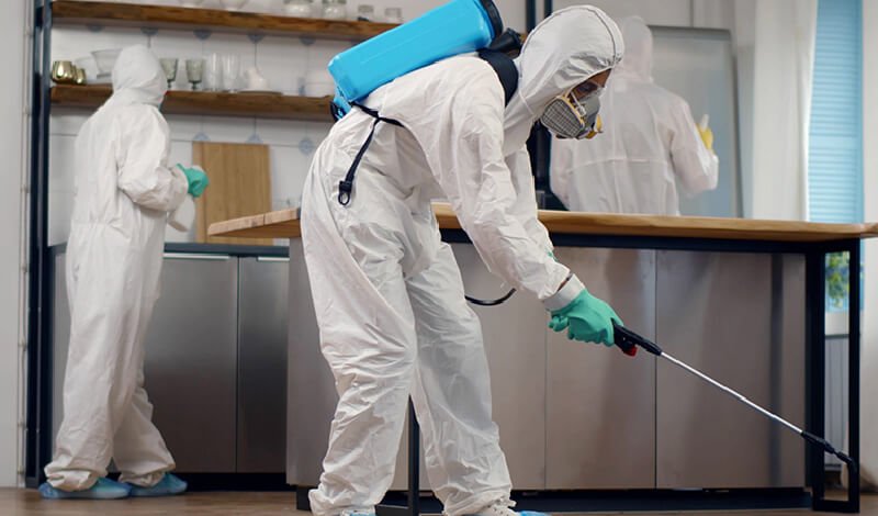 A cleaner in a white suit performing a sanitation service